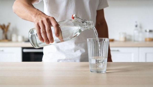 Person pouring water from swing-top bottle into ribbed glass on kitchen counter