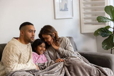 Warm family cuddling on couch under soft blanket enjoying movie night and bonding