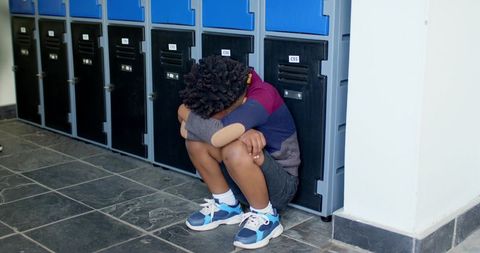 Child crouching introspectively in school hallway by lockers