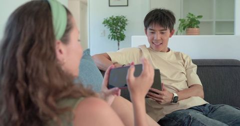 Couple relaxing on living room couch sharing tablet and smartphone, smiling together