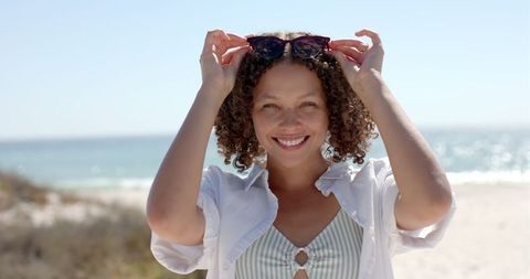 Cheerful Young Woman on Sunny Beach Holding Sunglasses