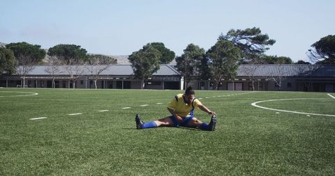 Young Woman Stretching on School Soccer Field Under Blue Sky