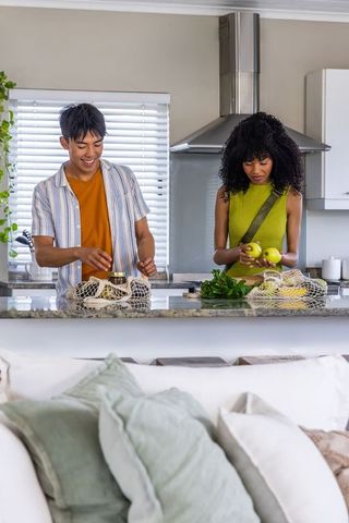 Diverse couple unpacking groceries at modern kitchen island using reusable mesh bags