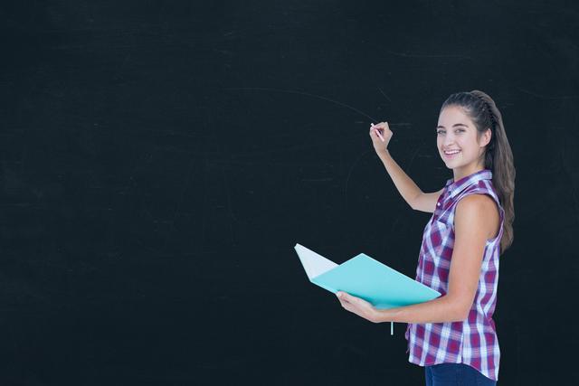 Digital composite of Side view of female student holding book while writing on blackboard