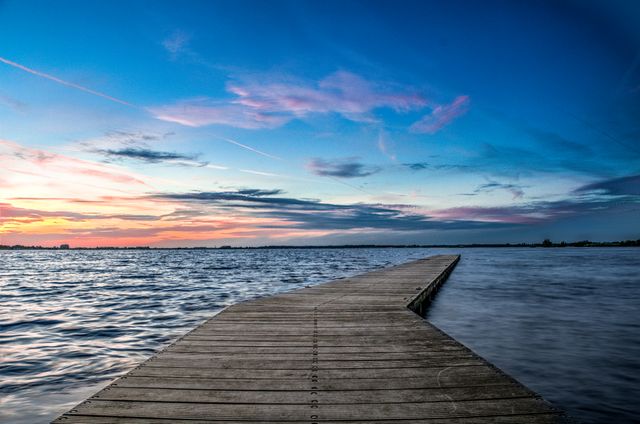 A wooden pier extending into a calm lake under a beautiful evening sky with shades of sunset colors. Ideal for travel blogs, nature and scenic posts, outdoor activity suggestions, and relaxation or mindfulness content.