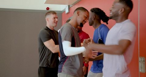 Diverse male athletes greeting and hugging in gym lobby showing teamwork and camaraderie