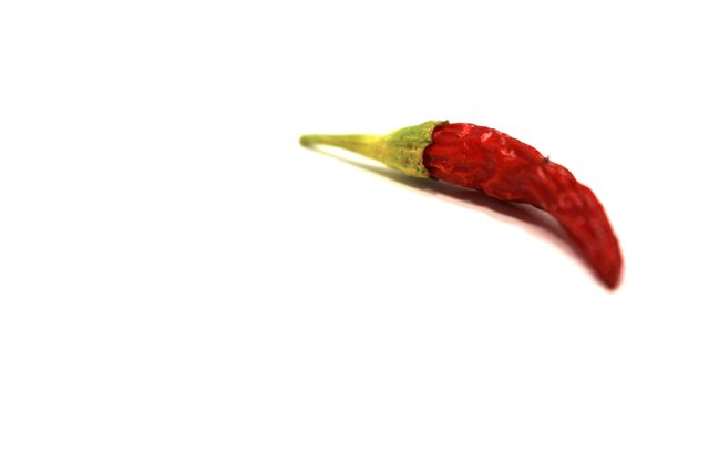 Close-up of a single red Thai chili pepper isolated on white background. The pepper shows vivid red color and natural texture, making it ideal for use in food blogs, culinary websites, recipe books, and health articles discussing spicy foods or ingredients.