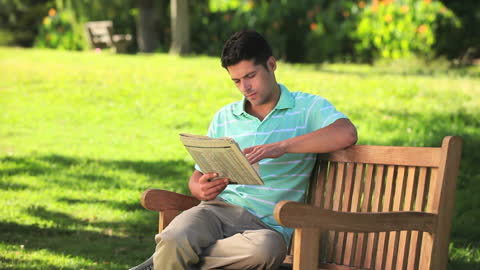 Man Relaxing on Park Bench Reading Newspaper