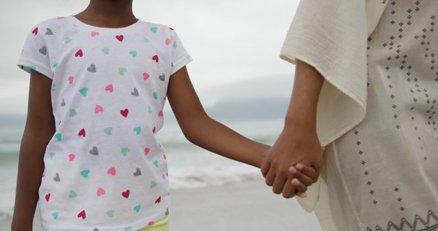 Midsection of african american mother and daughter holding hands on beach. Lifestyle, motherhood, childhood, summer, leisure and vacation.