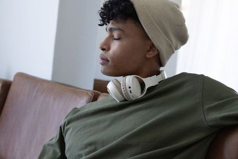Young african american man relaxing with headphones on leather couch beside sunlit window