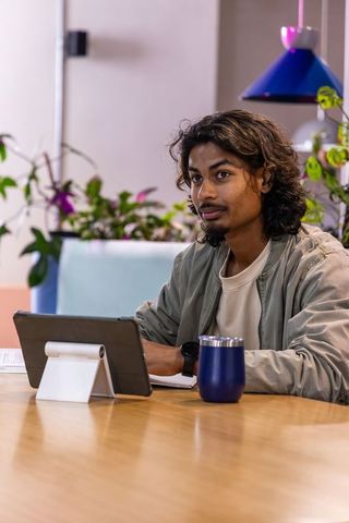 Young indian man working on tablet and writing notes in coworking lounge, focused
