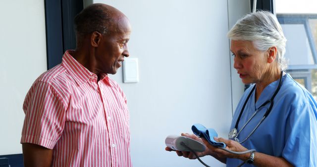 Senior male patient consulting with medical professional, likely discussing blood pressure results during a routine checkup. Ideal for healthcare, hospitals, elderly care advertisements, and patient education materials.