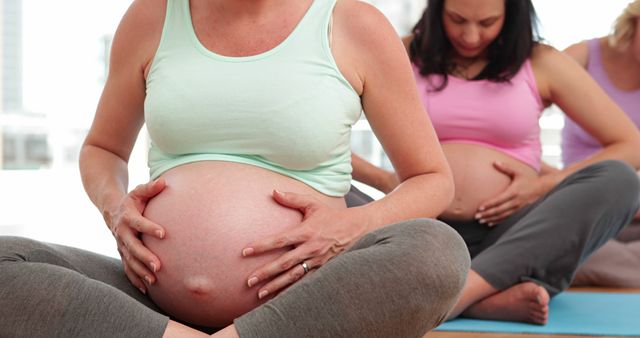 Pregnant women sitting on yoga mats, practicing prenatal yoga in group health class. Useful for promoting maternal health, fitness routines during pregnancy, prenatal care services, wellness programs for expectant mothers.