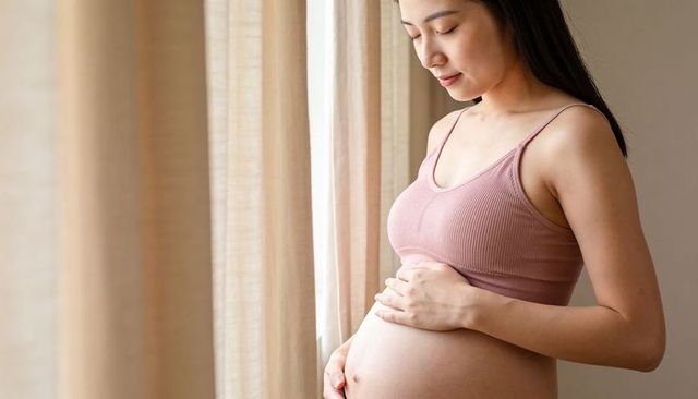 Expectant woman cradling baby bump by sunlit curtains, peaceful maternity reflection