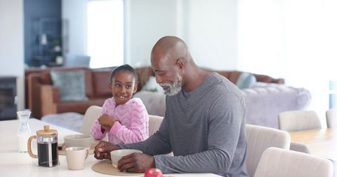 Grandfather and granddaughter sharing cozy morning coffee smiling during breakfast