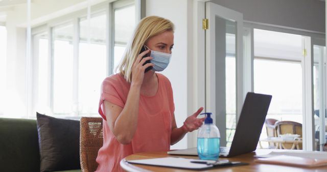 Woman Wearing Face Mask Talking on Phone while Working on Laptop at Home - Download Free Stock Images Pikwizard.com