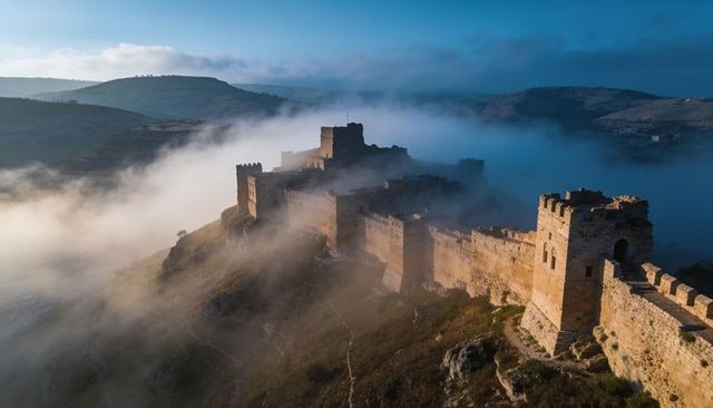 Sunlit medieval fortress rising through morning mist along rugged ridge