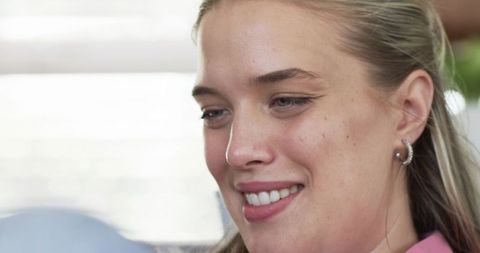 Closeup smiling young woman looking down with hair pulled back and silver hoop earring