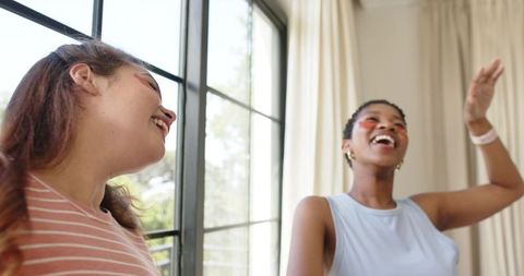 Friends laughing and celebrating with face paint and hoop earrings in sunlit living room