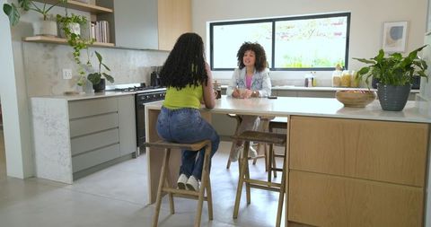 Women chatting at modern kitchen island with plants and natural light, lifestyle scene