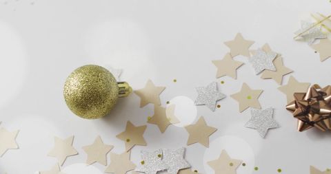 Golden bauble with star confetti on white background