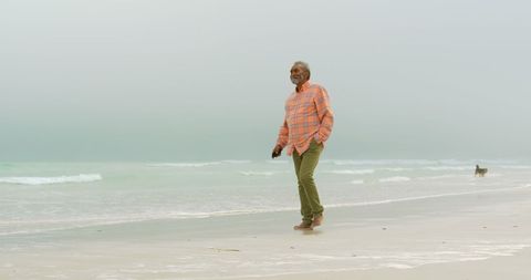 Senior Man Walking on Tranquil Beach Holding Mobile Phone