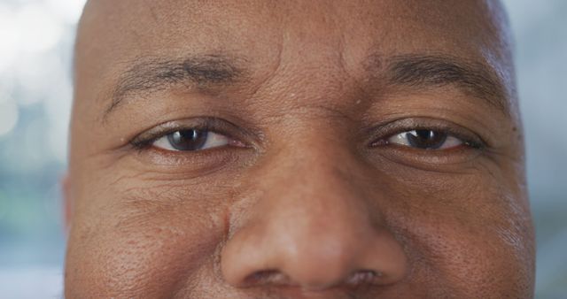 This photo captures the detailed texture of an African American man's face, with focus on his eyes and the bridge of his nose. The warm expression in his eyes conveys a sense of friendliness and approachability. Ideal for uses in diversity and inclusion campaigns, brochures displaying emotional warmth, or content emphasizing human connection.