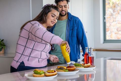 Couple preparing homemade burgers on kitchen island with condiments and drinks