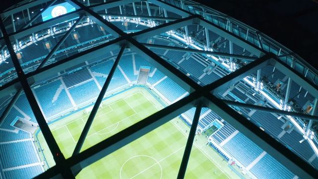 Framing high aerial night view of illuminated soccer stadium through roof truss