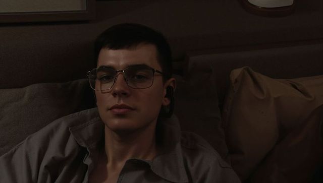 Young man reclining on couch wearing glasses and earbud in moody ambient light