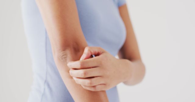 Woman gently scratching her elbow due to skin irritation, suggesting discomfort from a possible skin condition like dermatitis or an allergy. Perfect for use in healthcare, dermatology articles, skincare product advertisements, or educational materials on skin conditions and treatments.