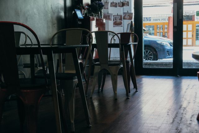 Interior of a cozy cafe showcasing a tranquil atmosphere with rustic chairs lined by large windows. Wooden floor adds to the warm ambiance. Ideal for use in websites, blogs, or advertisements focused on urban cafes, morning routines, or charming interiors.