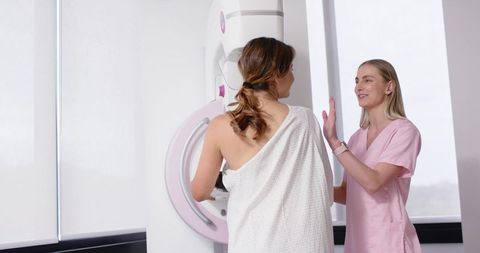 Woman undergoing mammogram while radiology technologist assisting at modern clinic