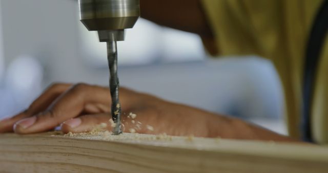 Close-up of a person drilling into wood at a workshop. Precision and safety are key in this woodworking project.