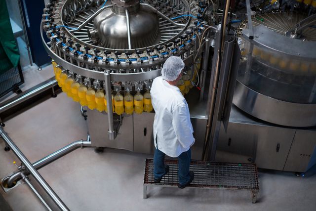 Factory engineer monitoring juice bottles on production line in a beverage manufacturing facility. Ideal for use in articles about industrial automation, manufacturing processes, quality control in food and beverage industry, and technological advancements in production lines.