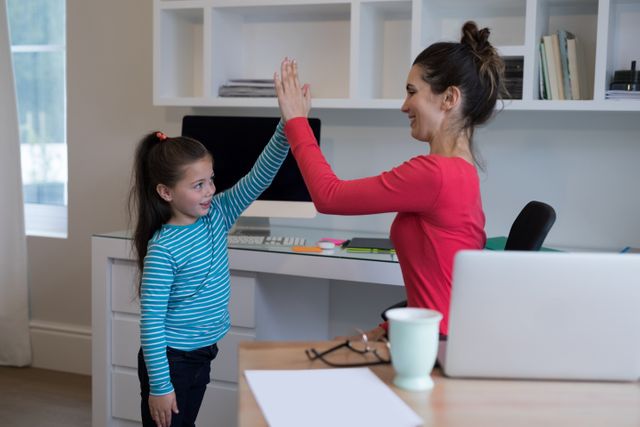 Mother and daughter giving high five to each other at home