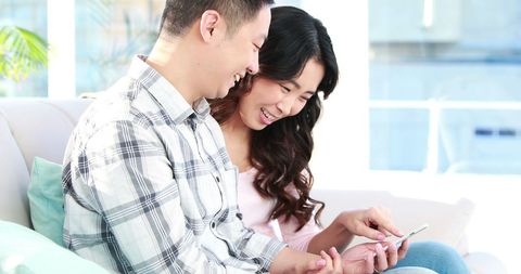 Joyful Asian Couple Laughing Together While Using Smartphone in Cozy Living Room - Download Free Stock Images Pikwizard.com