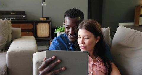 Interracial Couple Relaxing on Sofa Using Tablet for Streaming and Online Browsing