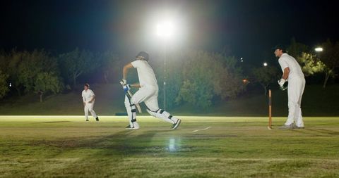 Night cricket match with batsman running between wickets under bright floodlights