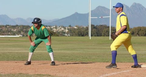 Two softball players guarding base while runner leading off on sunny amateur field