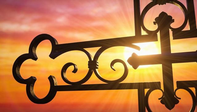 Sunrise through wrought-iron scrollwork with trefoil motif and radiant lens flare