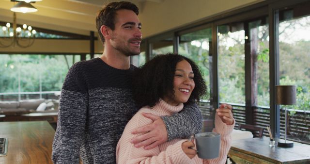 Happy diverse couple talking, embracing and drinking coffee in dining room. spending free time together at home.