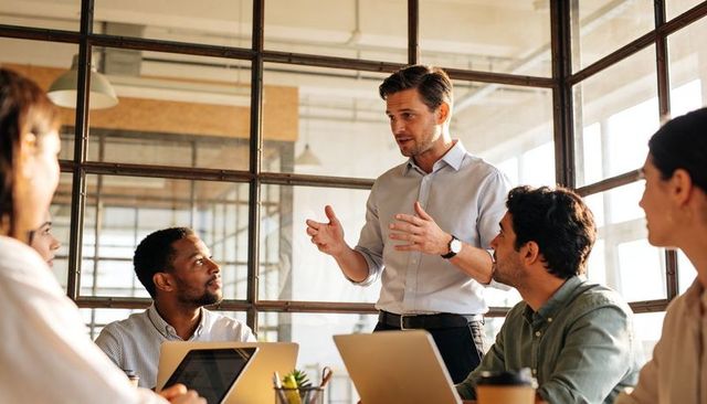 Team leader presenting strategy to diverse office team in glass conference room