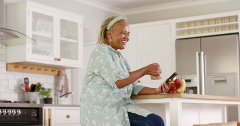 Senior Woman Using Smartphone at Kitchen Island, Happy and Engaged