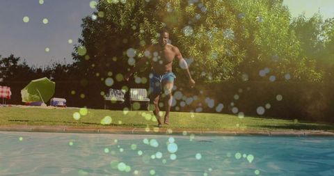 Shirtless man running toward pool on sunny backyard lawn with bokeh lens flare