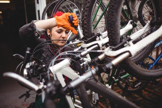 Mechanic wearing orange gloves repairing a bicycle in an industrial workshop. Ideal for themes such as professional repair services, bike maintenance, mechanical work, and DIY fixing tutorials.
