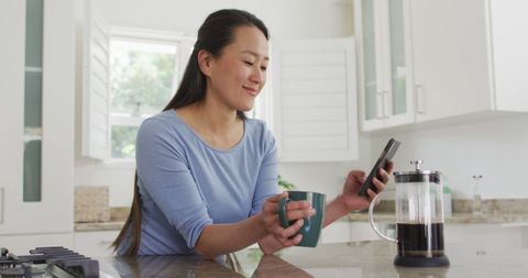 Asian Woman Relaxing with Coffee and Smartphone in Modern Kitchen - Download Free Stock Images Pikwizard.com