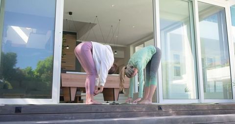 Two women stretching on sunlit patio steps practicing yoga warm-up in leggings