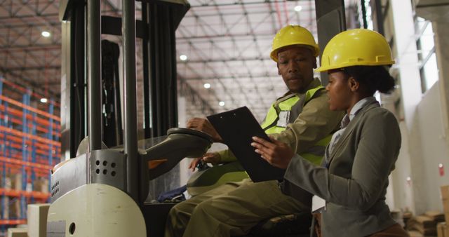 Warehouse foreman reviewing tasks with female manager, both involved in logistics and manufacturing. Ideal for representing warehouse operations, teamwork in industrial settings, and occupational safety practices.