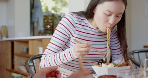 Young Woman Enjoying Meal with Chopsticks at Home